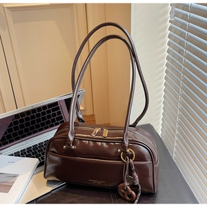 Détail du sac en cuir brillant marron foncé avec ferrures dorées et pendentif nœud