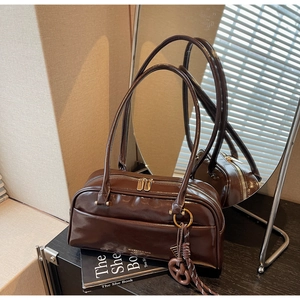 Détail du sac oreiller en cuir marron foncé poli avec zip doré et breloque tressée