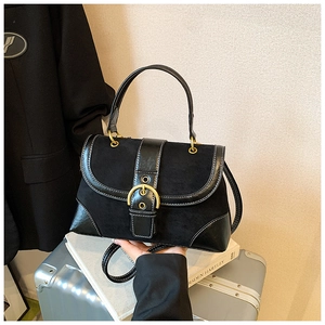 Detail of black suede saddle bag with golden metal buckle and smooth leather trim
