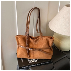 Détail du sac cabas en suédine marron avec double bandoulière sur un canapé en cuir noir