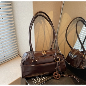 Détail d'un sac Boston en cuir brillant marron foncé avec fermeture éclair et breloque