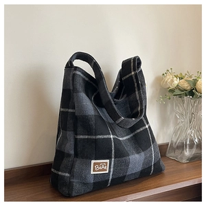 Close-up of black and grey plaid wool tote bag with brown leather bear patch on wood