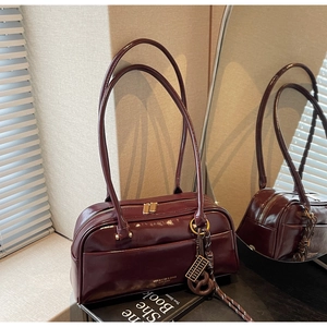 Détail du sac à main en cuir verni bordeaux avec zips dorés et breloque chic