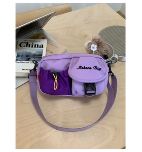 Detail of purple nylon crossbody bag with drawstrings, buckles and text logo on wooden desk