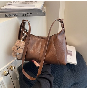Detailed view of brown retro leather shoulder bag with V-shaped stitching and bear charm