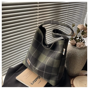 Close-up of a dark green plaid flannel tote bag with a woven Bear patch on the side