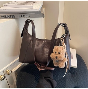 Detail view of coffee brown shoulder bag with vertical stitching and dog charm