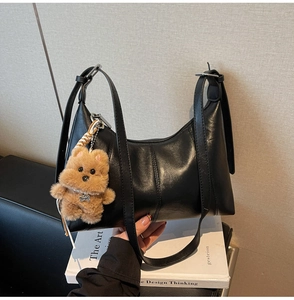 Detail of black leather hobo bag featuring a cute brown plush bear charm on white books