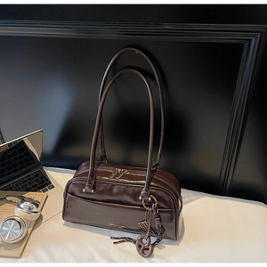Gros plan du sac oreiller en cuir verni café avec longues anses et détail du logo de marque