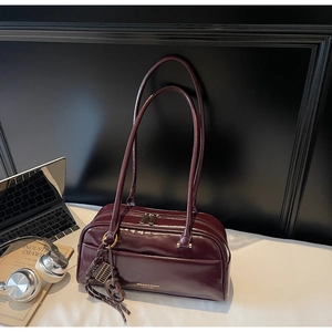 Détail du sac en cuir verni bordeaux avec logo doré et breloque en métal élégante