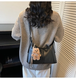 Detail of a black crescent shoulder bag with a cute brown plush bear charm accessory