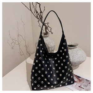 Detailed view of black leather tote bag with silver studs on a minimalist beige background