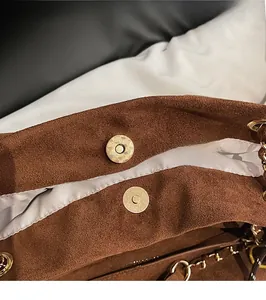 Détail du fermoir magnétique vintage sur sac bandoulière en daim marron et chaîne dorée