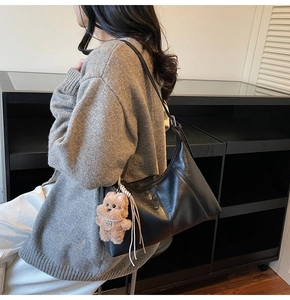 Side view of black minimalist underarm bag with cute plush bear charm on the strap