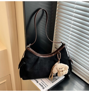 Détail du sac dumpling en daim noir avec bordure en cuir marron et breloque chiot