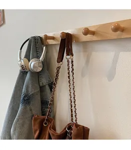 Sac seau en daim marron avec bandoulière chaîne en métal sur un crochet en bois