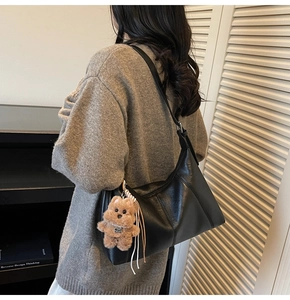 Detail of black matte PU leather shoulder bag with a cute brown plush bear pendant