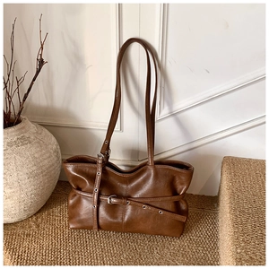 Détail d'un sac cabas en daim marron avec œillets argentés et lanière à boucle rétro