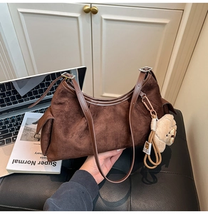 Texture détaillée du sac hobo en daim marron foncé avec sangle réglable et breloque ours