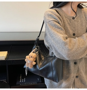 Detail of minimalist black leather underarm bag featuring a cute brown plush bear pendant