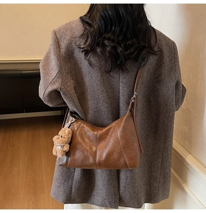 Close-up of retro brown leather shoulder bag with a cute plush bear charm decoration