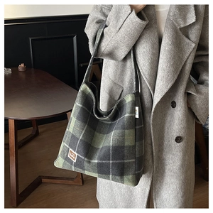 Detail of dark green checkered wool tote bag showing texture and leather logo tag