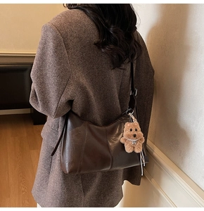Deep brown shoulder bag with plush bear charm on wool coat background for winter