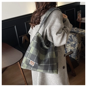 Macro detail of the forest green plaid tote bag showing warm wool-like texture and bear tag