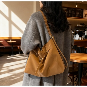 Detailed side view of a caramel brown leather hobo tote bag worn by a model in a cafe
