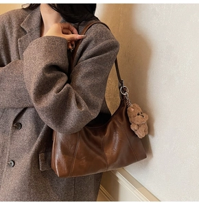 Detail of dark brown leather underarm bag featuring decorative stitching and plush bear charm