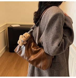 Detail of dark brown vintage faux leather shoulder bag with a cute plush bear charm
