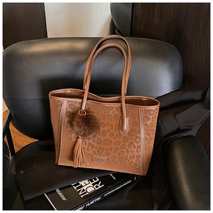Detail of large leopard print tote bag with plush ball and tassel charm on a sofa