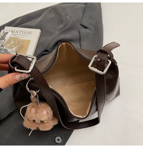 Detail view of deep brown leather bag showing spacious interior and plush bear charm