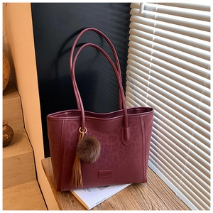 Detail of burgundy tote bag with leopard embossing, tassel charm, and plush ball