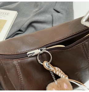 Detail of dark brown leather handbag with metallic zipper and a cute plush charm