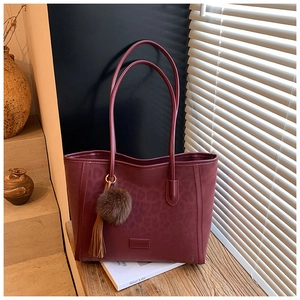 Close-up of wine red leopard tote bag with a faux fur pompom and leather tassel charm