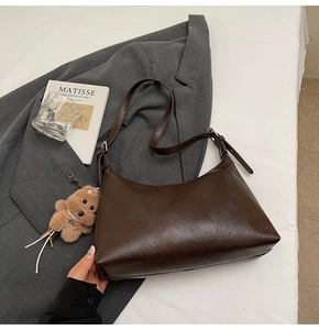 Detail of dark brown hobo bag with adjustable strap and cute bear charm on white bedding