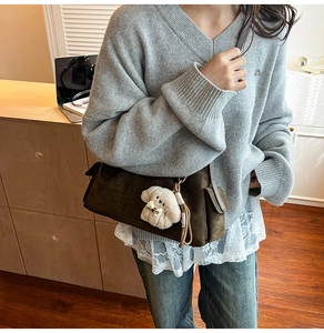 Détail d'un sac bandoulière en daim marron avec poche latérale et breloque chien peluche