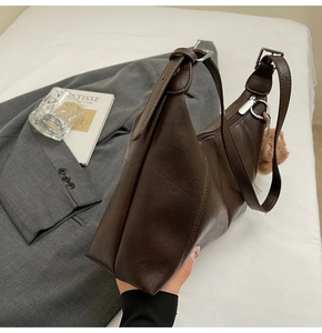 Close-up of brown faux leather shoulder bag featuring pebbled texture and bear charm