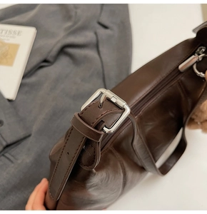 Close-up of dark brown leather handbag with silver buckle detail and smooth zipper