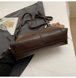 Detail view of dark brown leather shoulder bag featuring stitching and bear charm accessory
