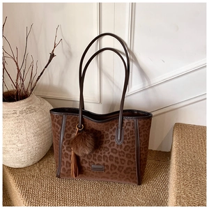 Detail of leopard print tote bag with plush pom-pom charm and tassel pendant accessory