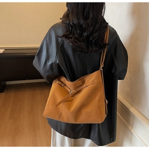 Rear view of a caramel leather tote bag with metallic ring buckle worn on shoulder
