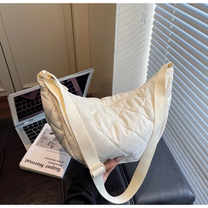 Detailed view of quilted cream nylon crescent bag on a minimalist desk with laptop and books