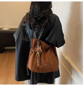 Détail du sac seau marron en daim avec chaîne et breloque ours porté par un mannequin
