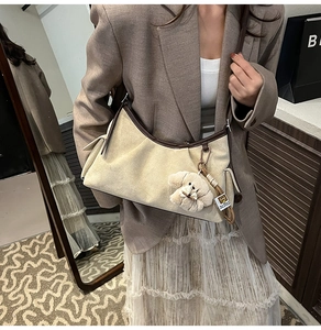 Détail du sac bandoulière en toile beige avec bordure en cuir marron et breloque chien