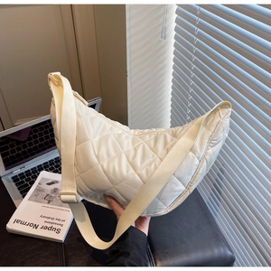 Detail of cream quilted nylon crescent bag with adjustable wide strap on work desk