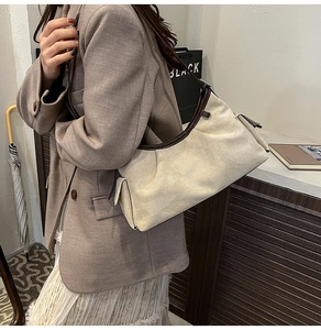 Détail du sac bandoulière blanc cassé avec bordure brune et poche latérale sur un mannequin