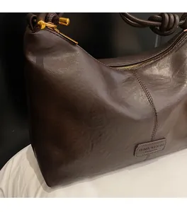 Detailed view of dark brown leather tote bag with knotted handle and gold metal zipper