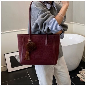 Detail of burgundy leopard print tote bag with brown pompom and brand logo label